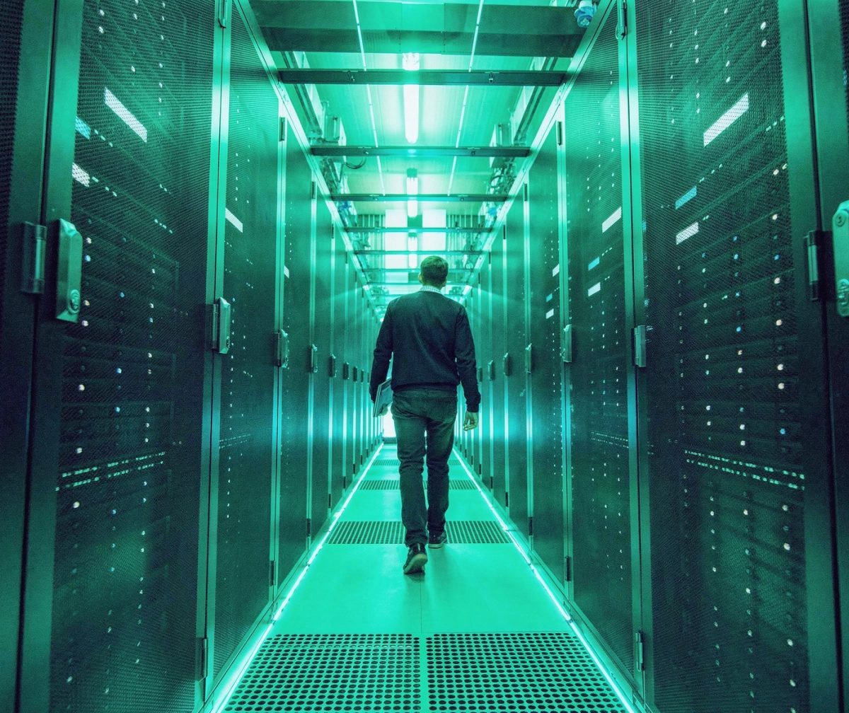 A person walks down an aisle between rows of servers in a data center.