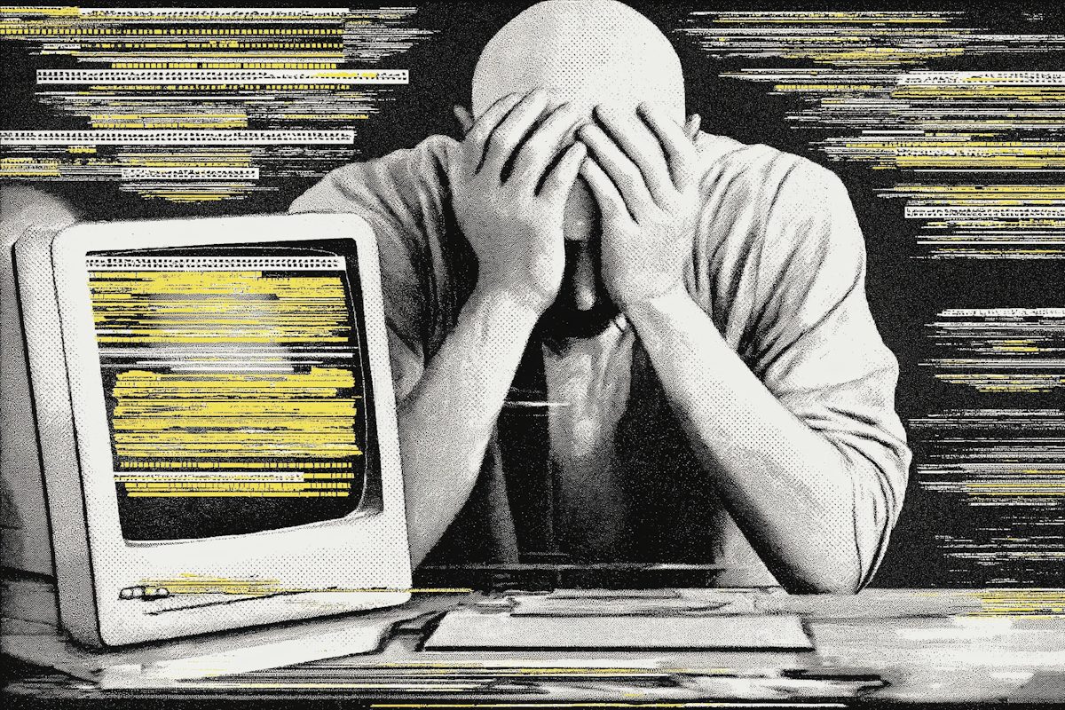 A person holds their head in their hands in front of an old computer screen full of lines of text.