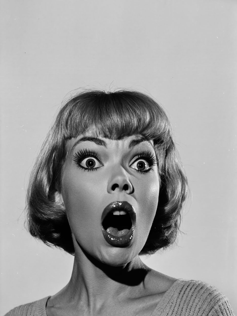 A woman staring open-mouthed in shock. A black-and-white picture in a 1960s studio style.